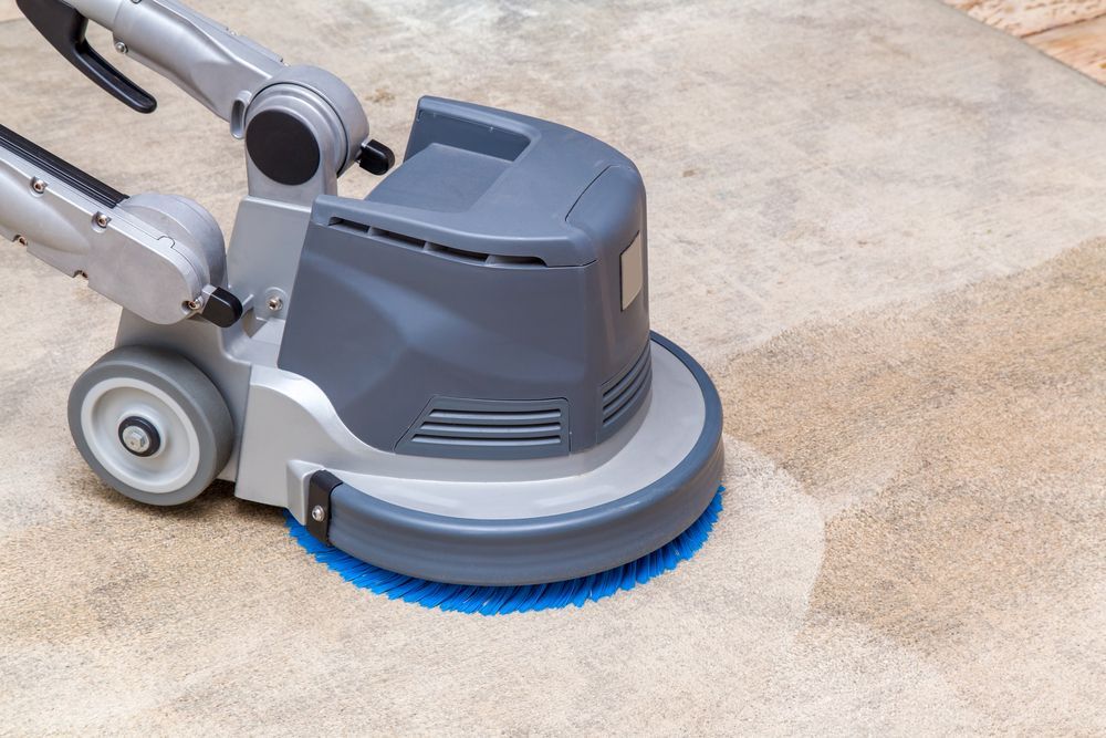 Gray Floor Scrubber with Blue Brushes Cleaning a Concrete Surface Outdoors — Broadbeach Carpet Cleaning In Broadbeach, QLD