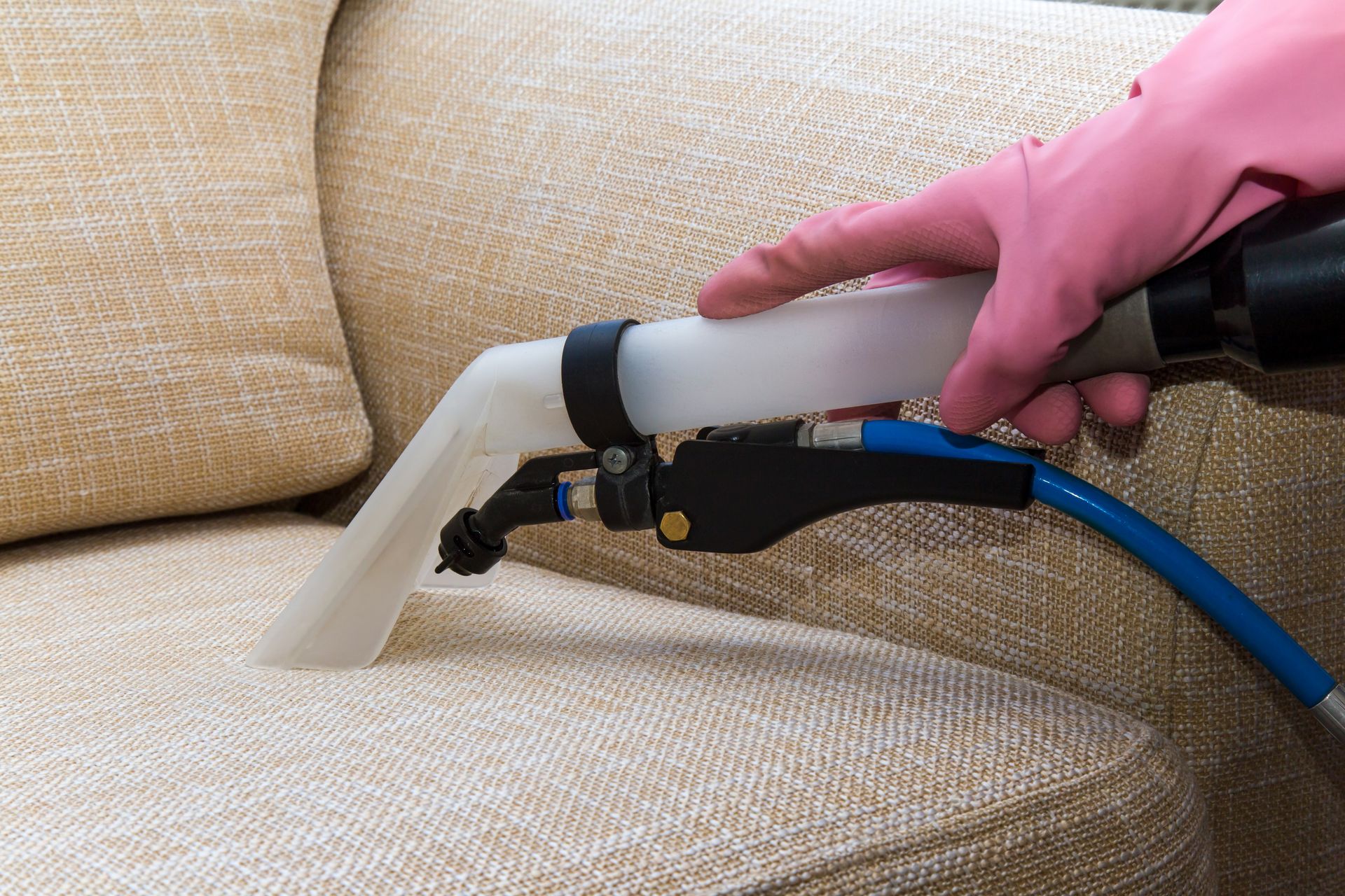Hand using a carpet cleaning nozzle on a beige couch cushion — Broadbeach Carpet Cleaning In Main Beach, QLD