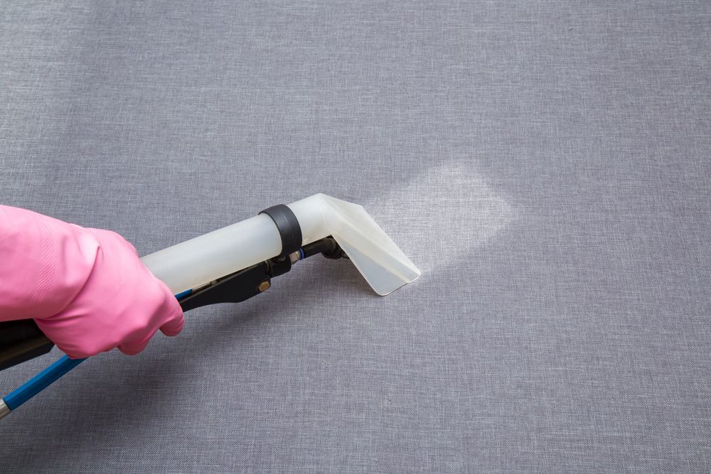 Gloved Hand Using a Steam Cleaner on A Gray Fabric Surface — Broadbeach Carpet Cleaning In Broadbeach, QLD