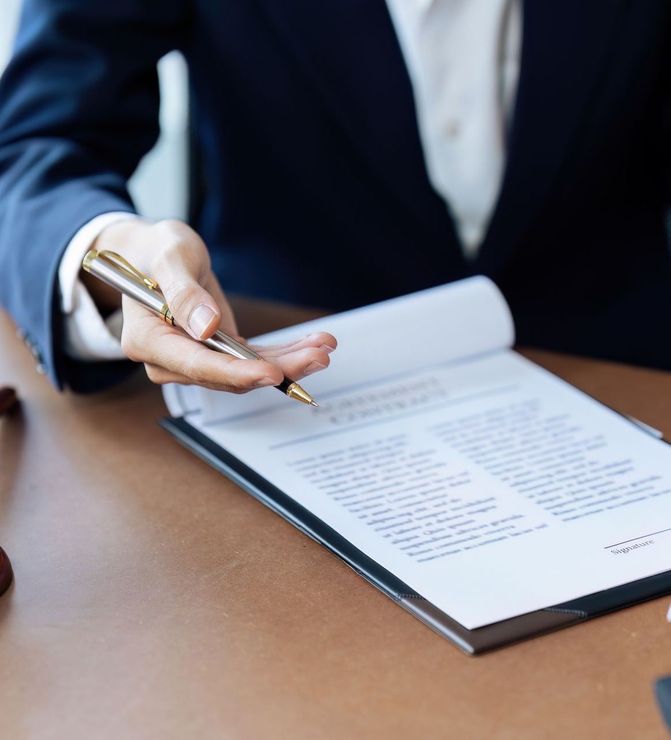 Person in suit points to a document with a pen at a desk.