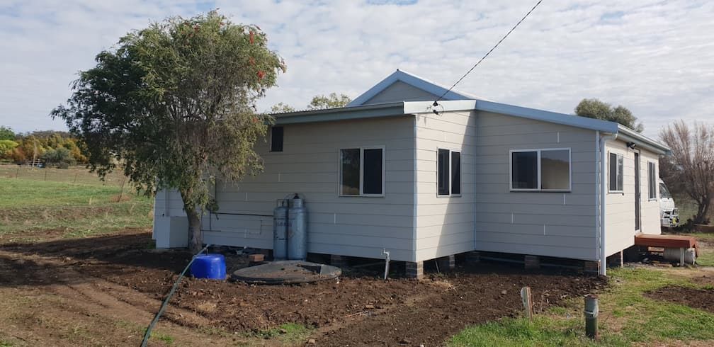 A Small White House Is Sitting in The Middle of A Field — Edwards & Froud Building Services Pty Ltd in Tamworth, NSW