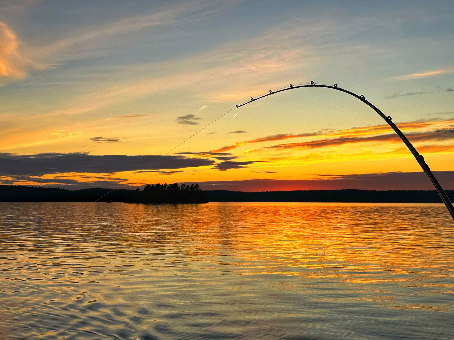 Sunset over a calm lake with orange sky and a silhouetted fishing rod at the right edge