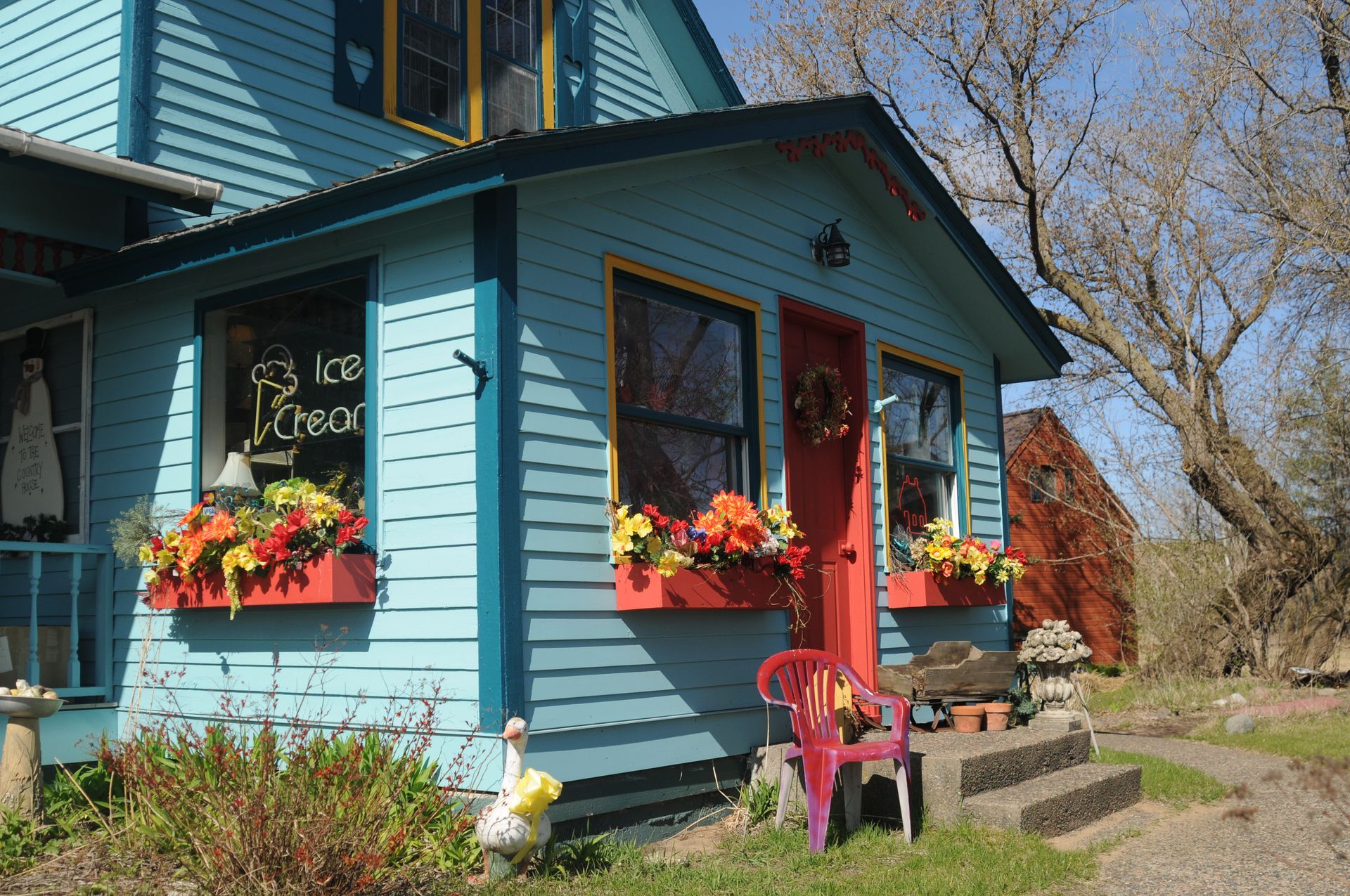 Blue cottage with red door, flower boxes, and a small porch in a sunny yard