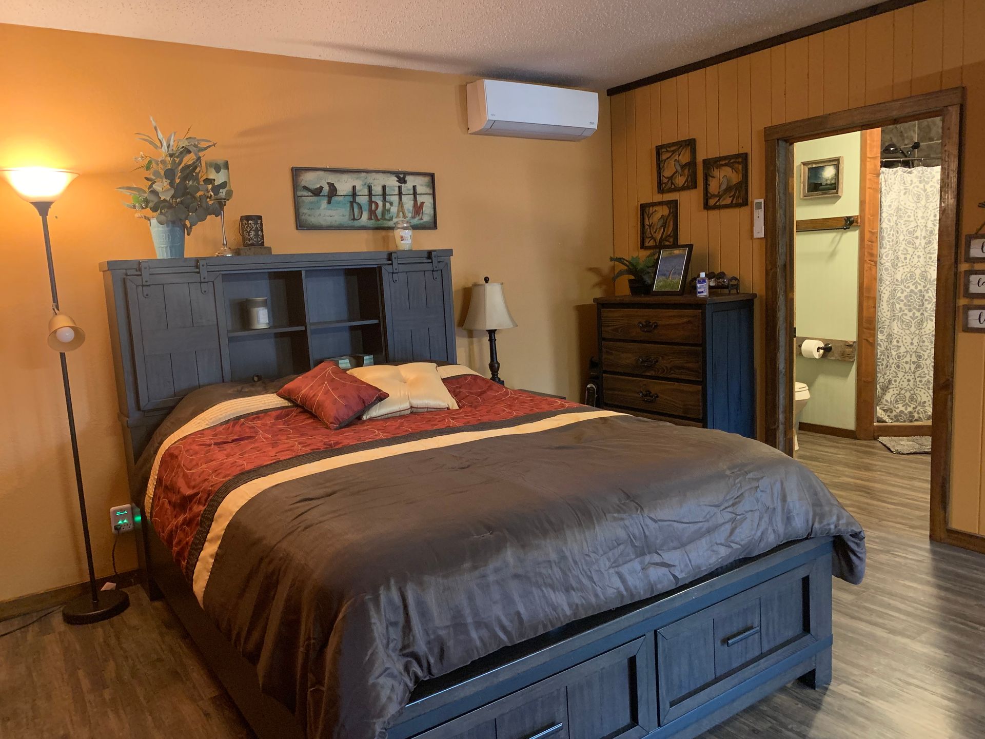 Cozy bedroom with a large bed, dark wood furniture, warm lighting, and an open doorway to a bathroom.