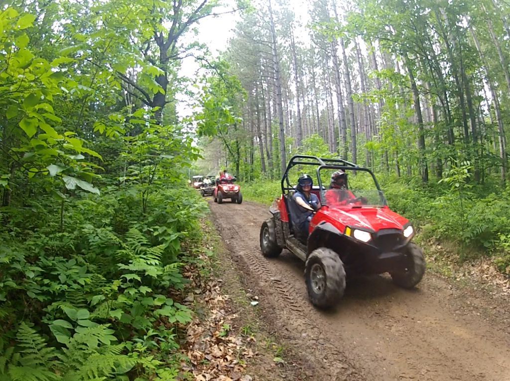 Two red off-road vehicles driving on a muddy forest trail