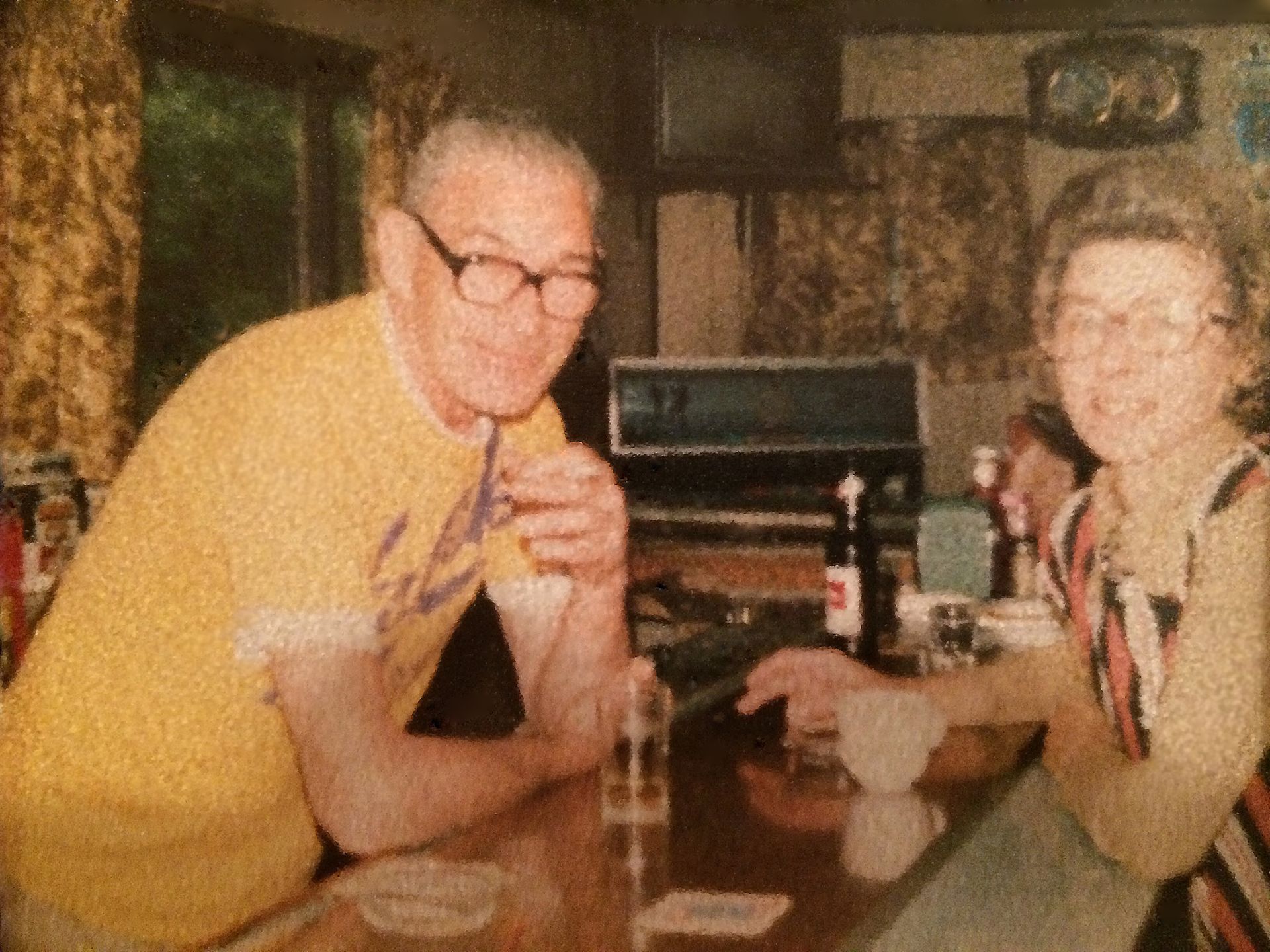 Two people seated at a restaurant table, smiling and raising drinks in a casual indoor setting.