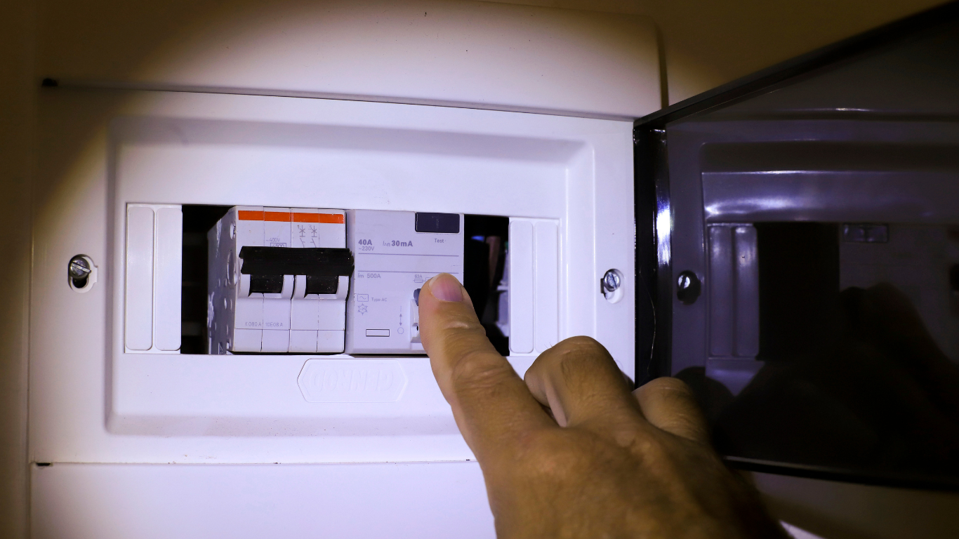 Hand turning on a circuit breaker in an electrical panel inside a wall recess