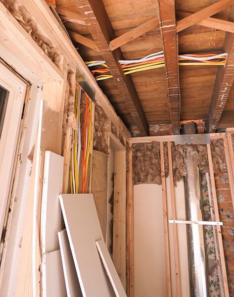 Partially stripped interior wall and ceiling framing in a renovation area, with exposed beams and wires.