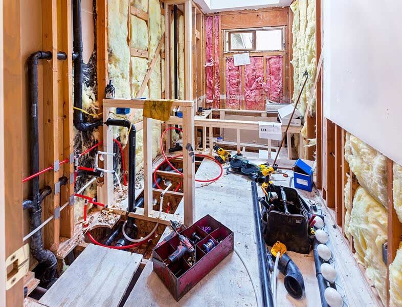 Basement under renovation with exposed studs, insulation, tools, and construction materials scattered on the floor.