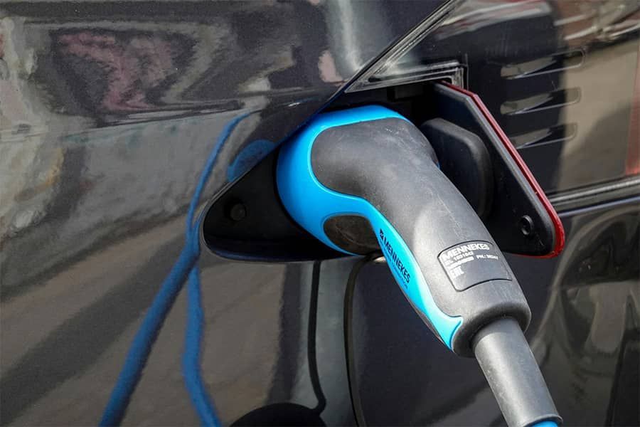 Electric car charging plug connected to a vehicle charging port, with a blue and gray connector and cable.
