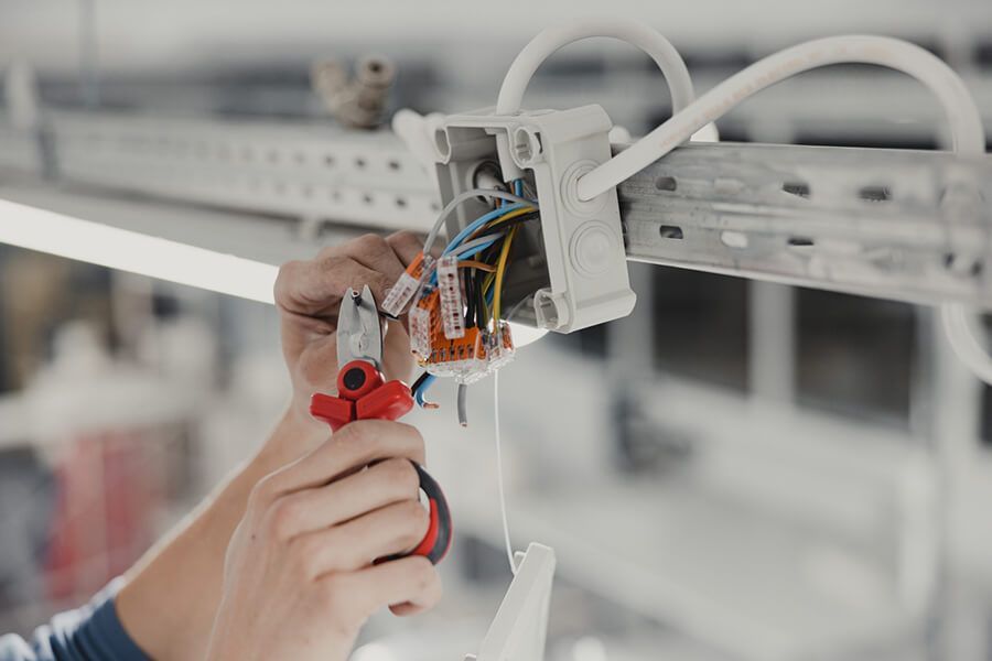 Hands wiring an electrical junction box with pliers in a workshop.