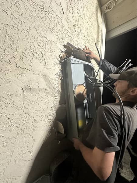 Worker installing a wall-mounted unit beside a textured exterior wall
