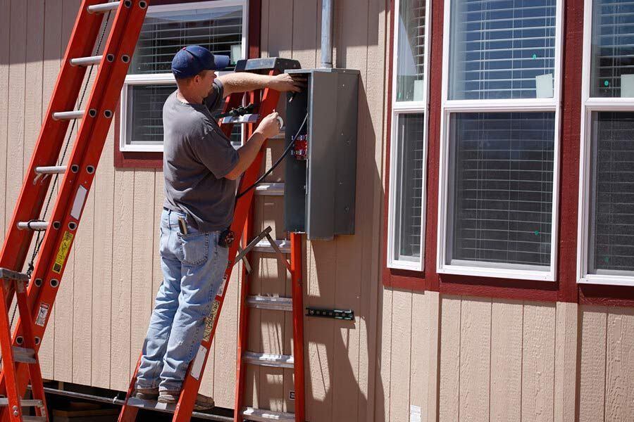 Worker on ladder installing an electrical panel on the side of a house