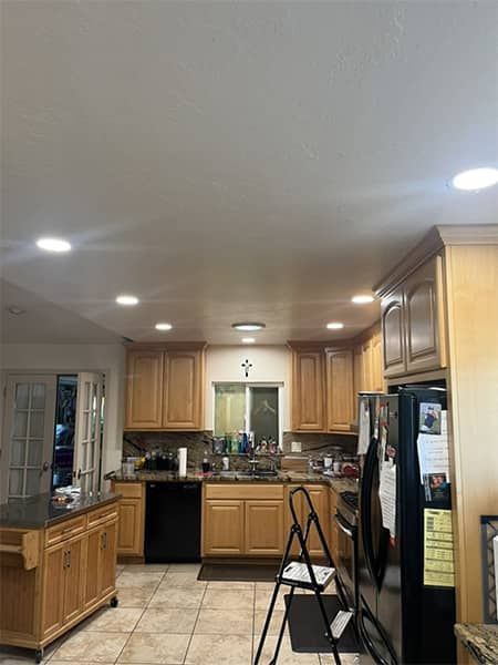 Bright kitchen with wood cabinets, tiled floor, black appliances, and a small step ladder in the foreground