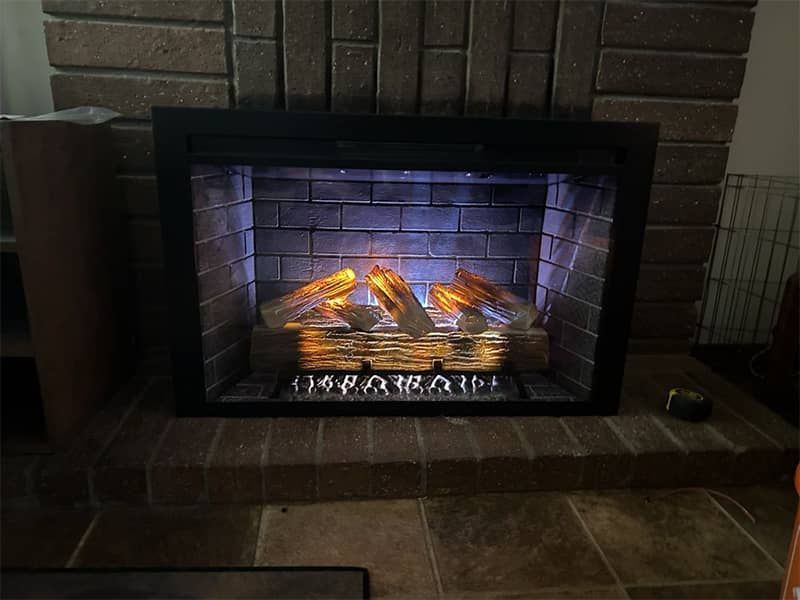 Electric fireplace with glowing logs set into a brick hearth in a tiled living room.