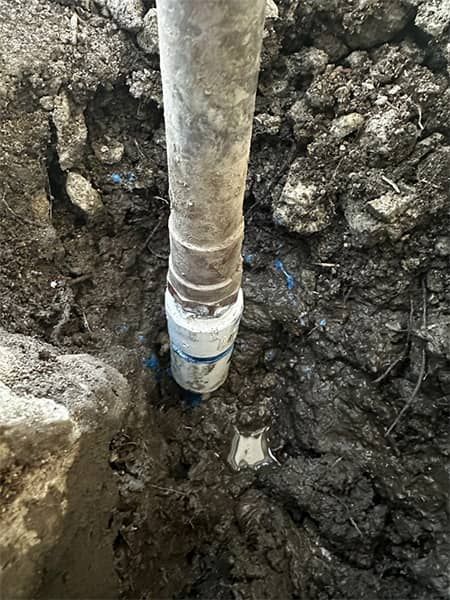 White pipe in muddy excavation hole with wet soil around it