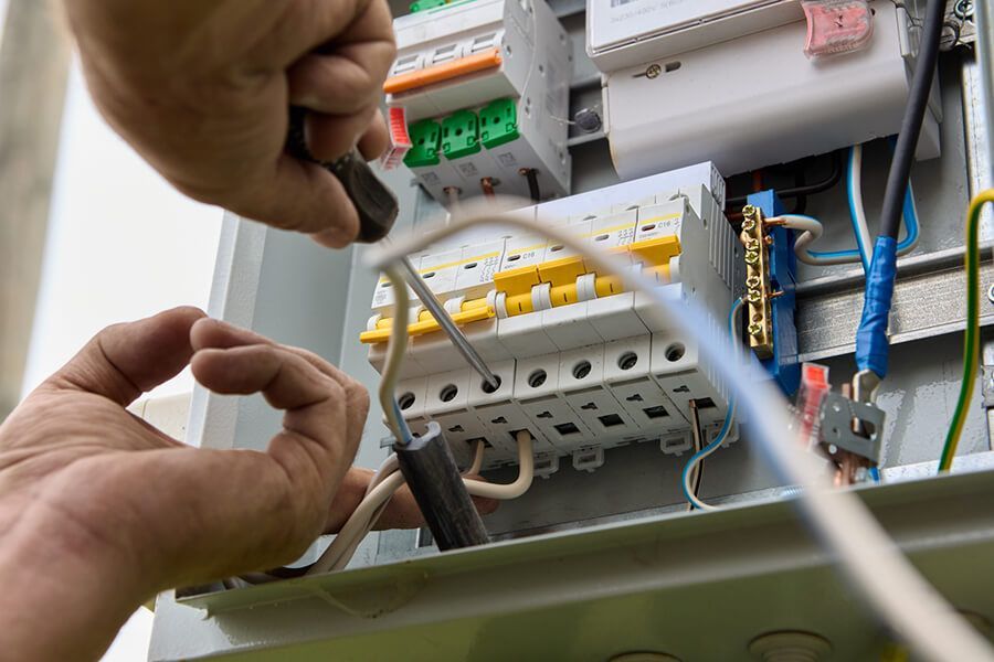 Hands wiring an electrical panel with circuit breakers and cables
