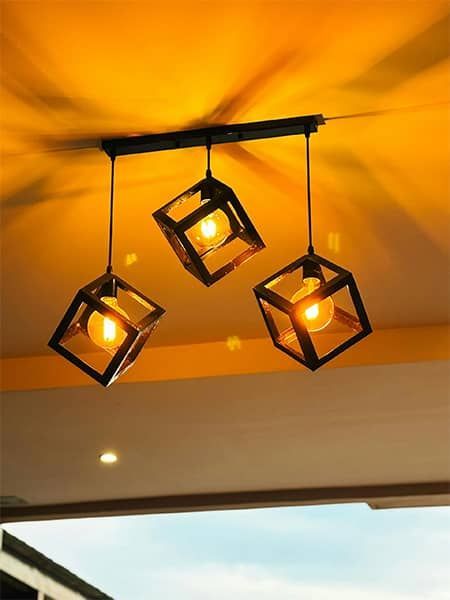 Three black cube pendant lights with warm bulbs hanging from a ceiling with orange glow