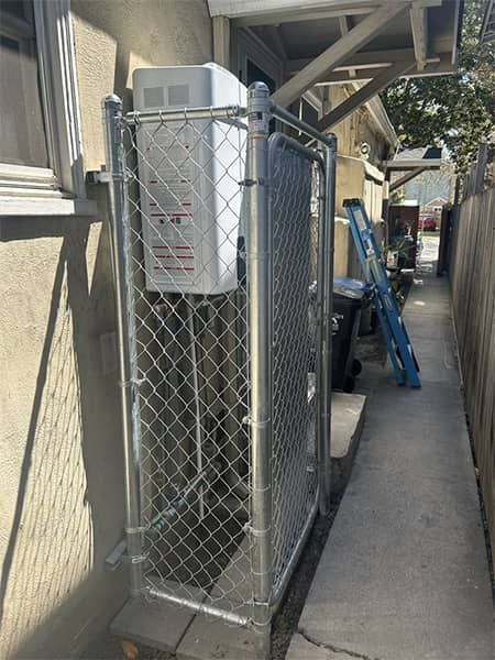 Chain-link fenced enclosure with outdoor HVAC equipment beside a narrow walkway under a building overhang