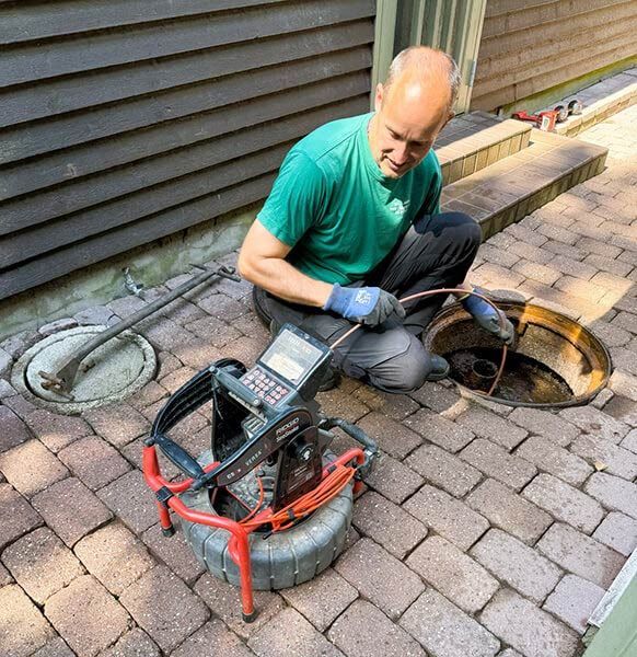 Technician inspecting a sewer drain with a handheld camera on a brick patio outdoors
