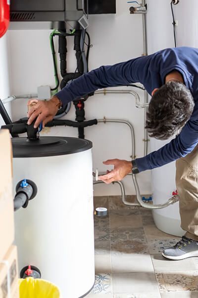 Technician adjusting pipes on a white water heater in a utility room