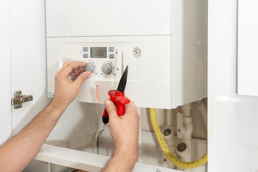 Hands adjusting a wall-mounted boiler with red pliers and a screwdriver