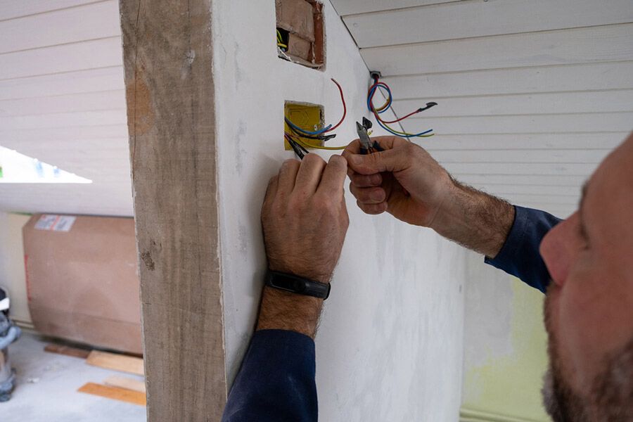 Electrician wiring an electrical box in a wall, handling exposed colored wires.