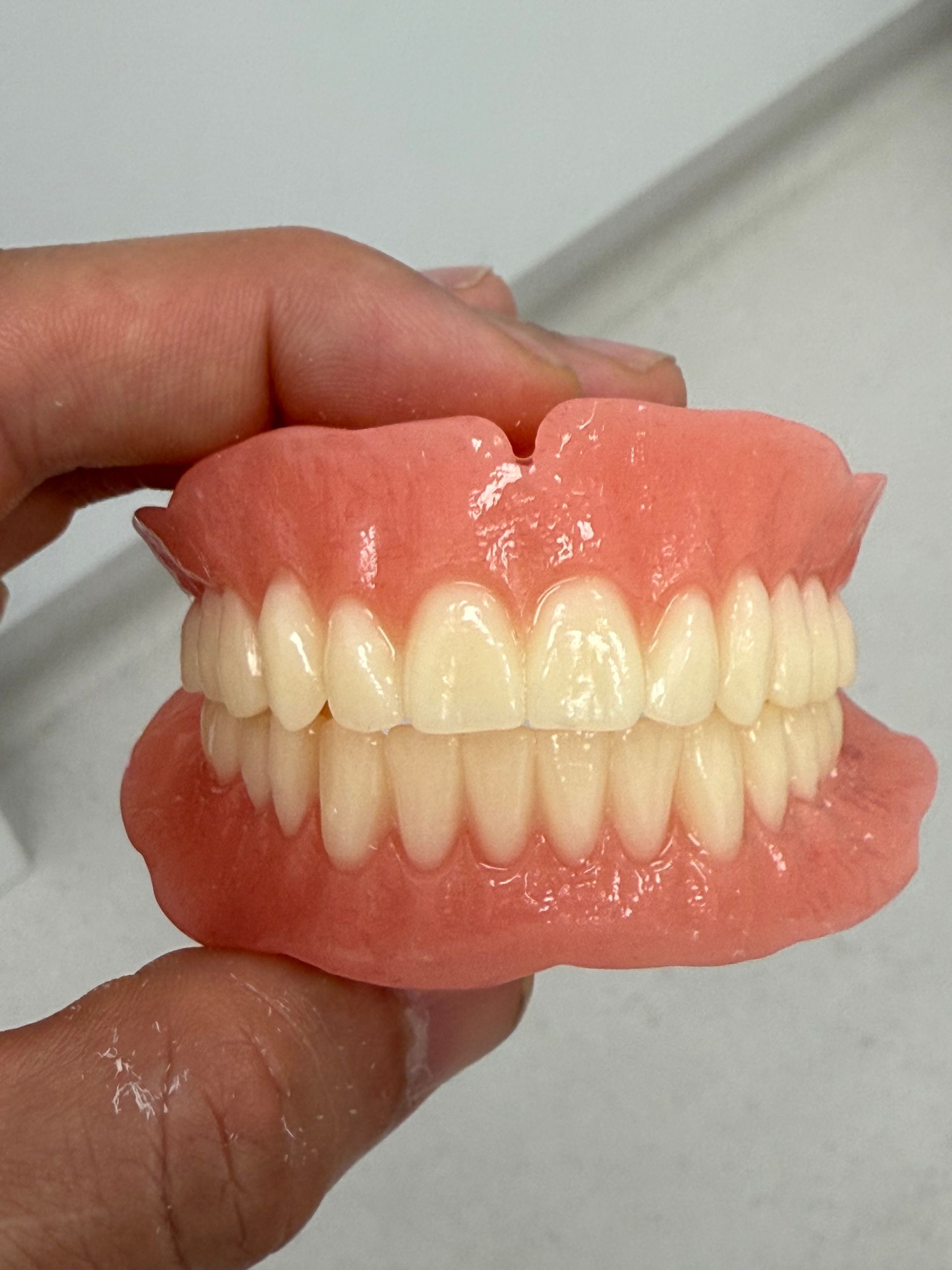 A set of full dentures, pink gums, and white teeth, held in a person’s hand— Dentures Direct Ballina In Ballina, NSW