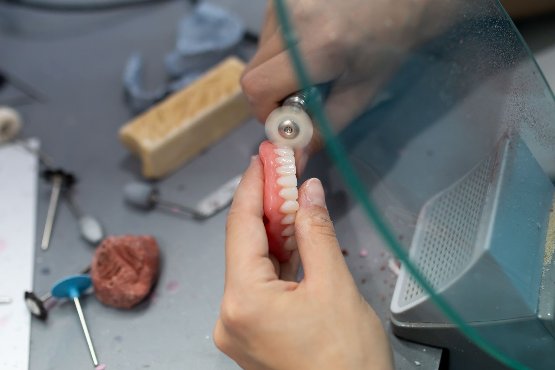 Hands holding a set of false teeth being polished with a rotary tool in a dental lab— Dentures Direct Ballina In Ballina, NSW