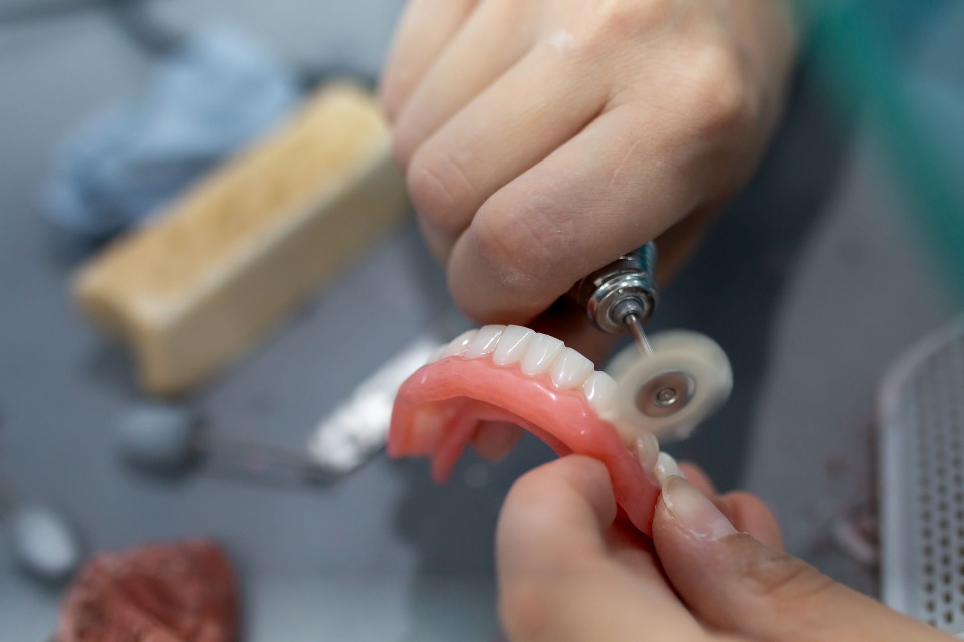 Person polishing dentures with a rotary tool in a lab setting.— Dentures Direct Ballina In Ballina, NSW