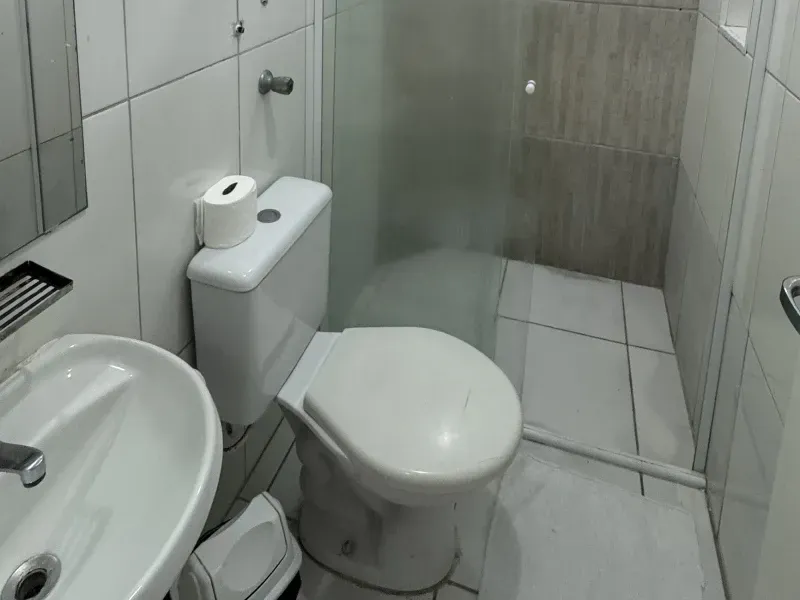 Um banheiro pequeno e moderno com pia branca, vaso sanitário branco com rolo de papel higiênico e box de vidro para o chuveiro.