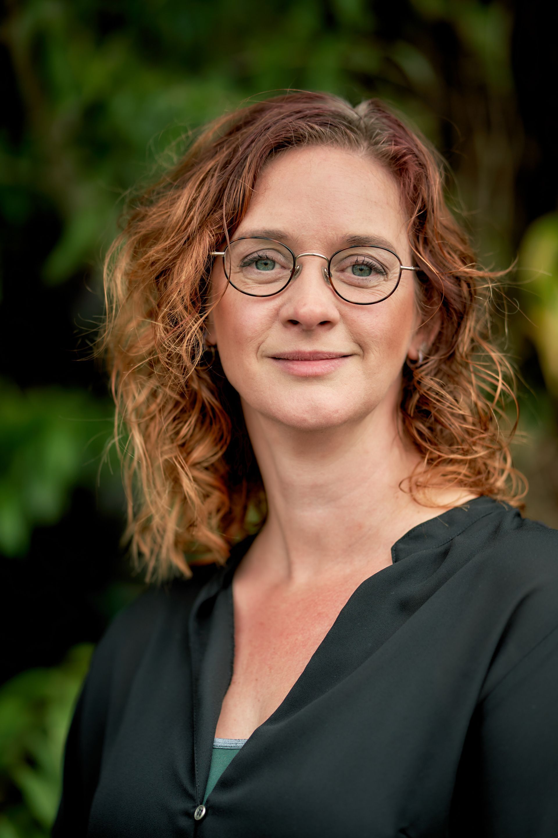 Een vrouw met een bril en een zwart shirt lacht naar de camera.