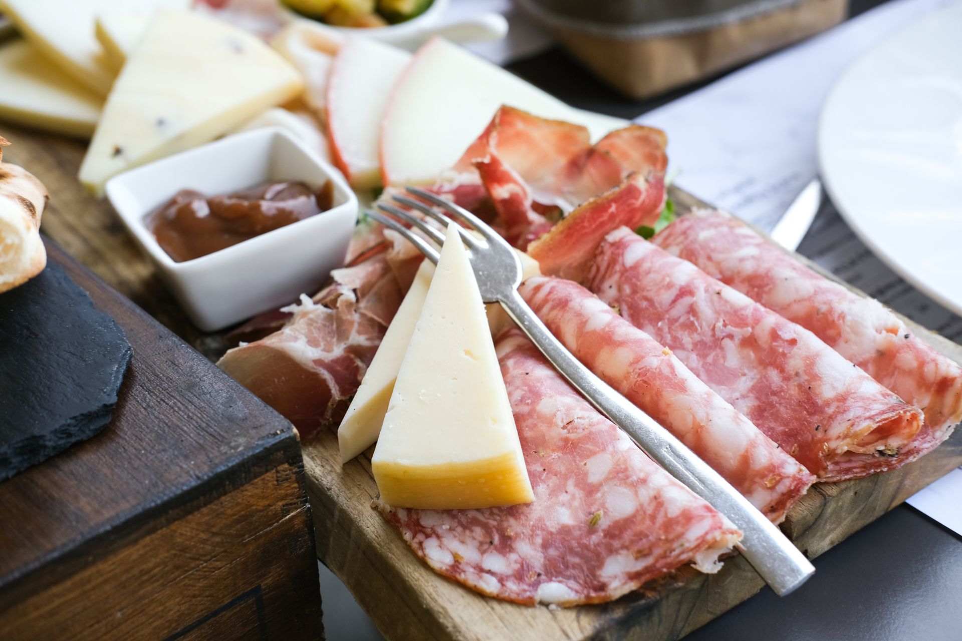 Un tagliere di legno con sopra carne e formaggio e una forchetta.