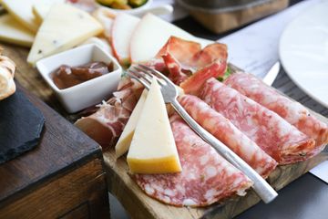 Un tagliere di legno con sopra carne e formaggio e una forchetta.