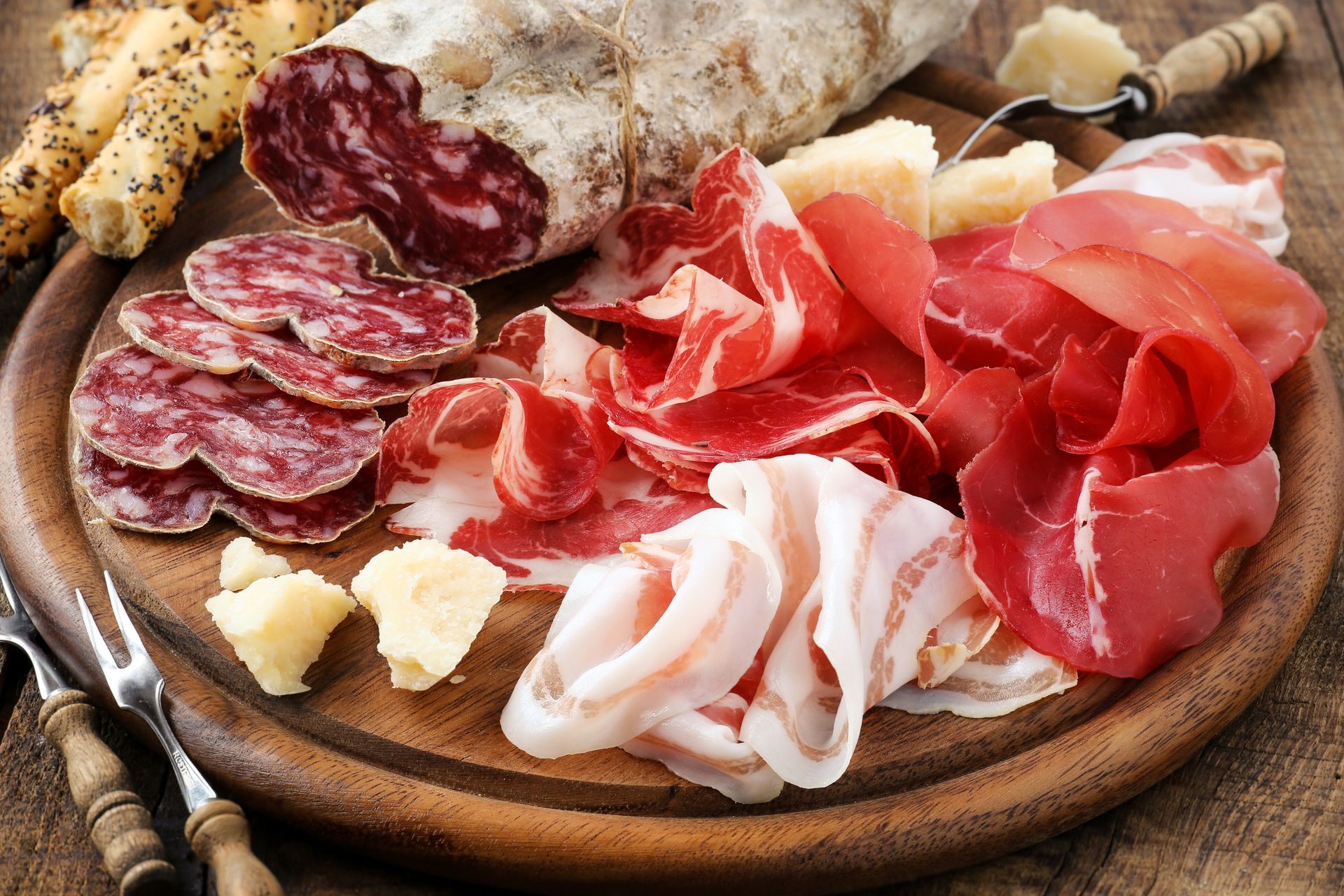 Un tagliere di legno sul quale vengono disposti vari tipi di carne e formaggi.