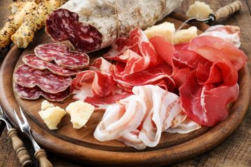 Un tagliere di legno sul quale vengono disposti vari tipi di carne e formaggi.