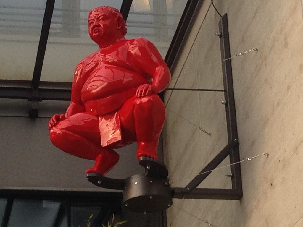 Une statue rouge d'un homme accroupi sur un poteau