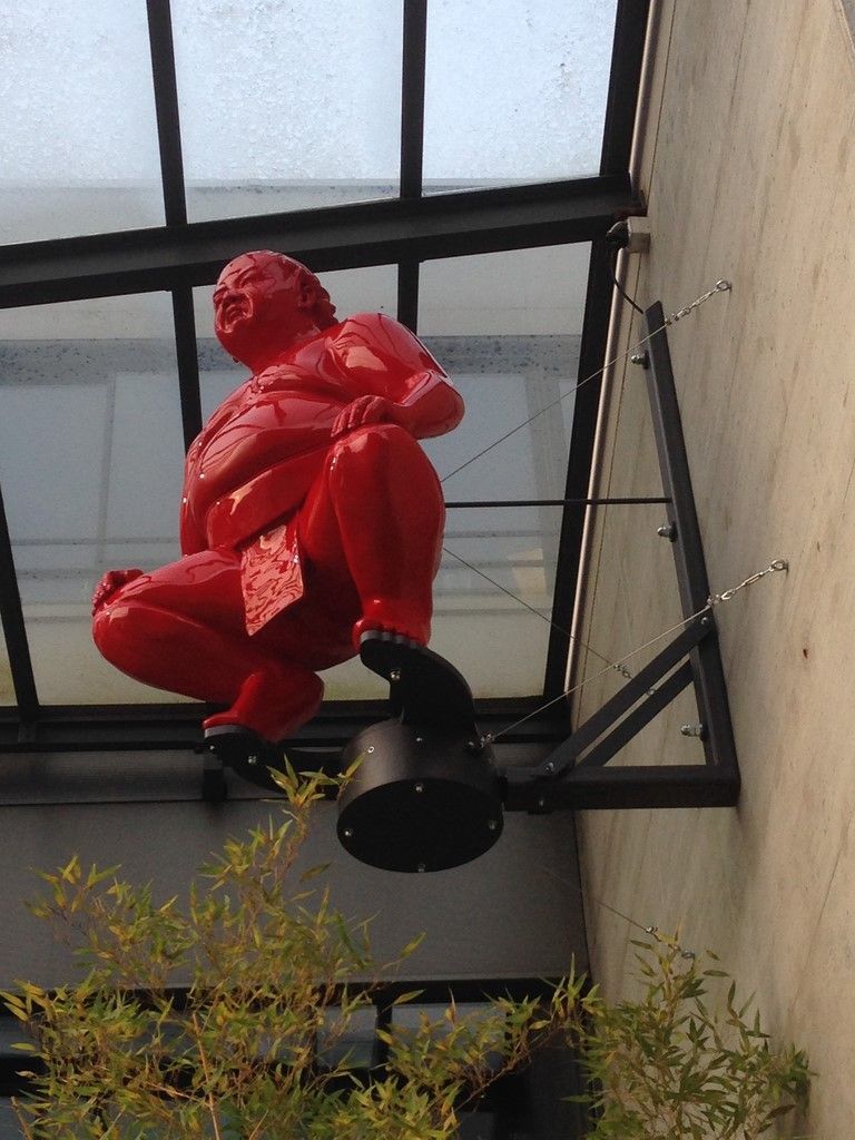 Une statue rouge d'un homme est suspendue au côté d'un bâtiment
