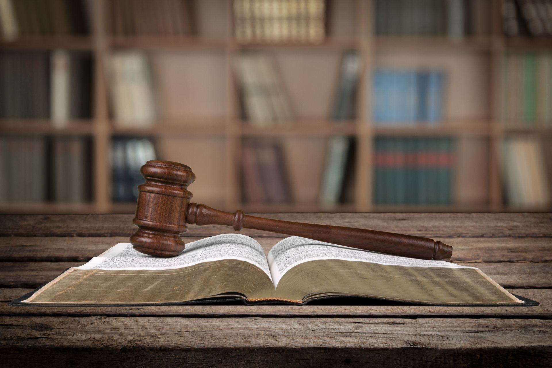 A wooden judge 's gavel is sitting on top of an open book on a wooden table.