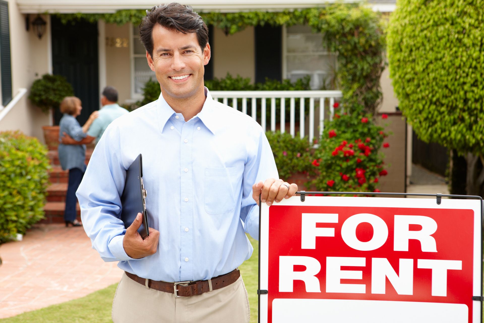 A man is holding a for rent sign in front of a house