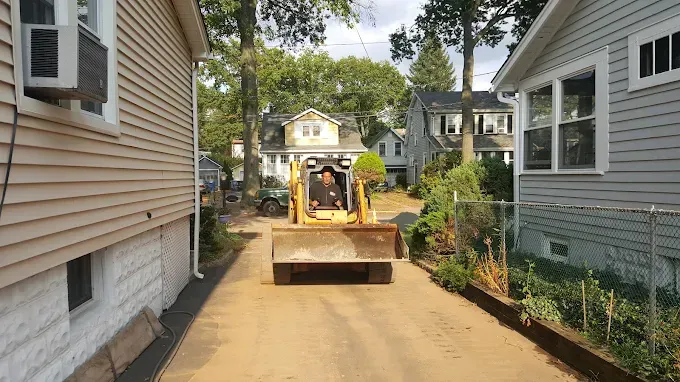 A bulldozer is driving down a dirt road between two houses.