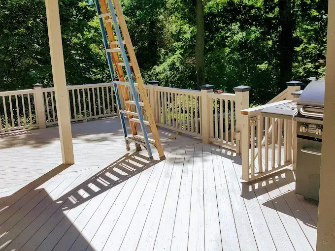 A ladder is sitting on top of a wooden deck next to a grill.