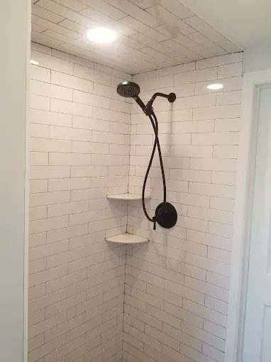 A shower with white tiles and a black shower head.