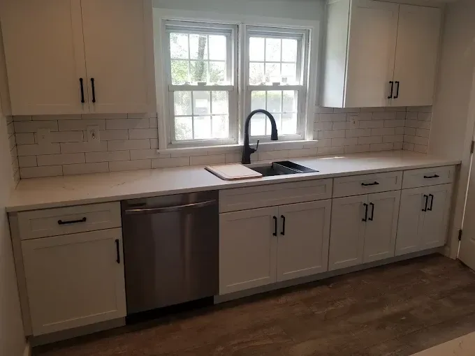 A kitchen with white cabinets , stainless steel appliances , a sink and a window.