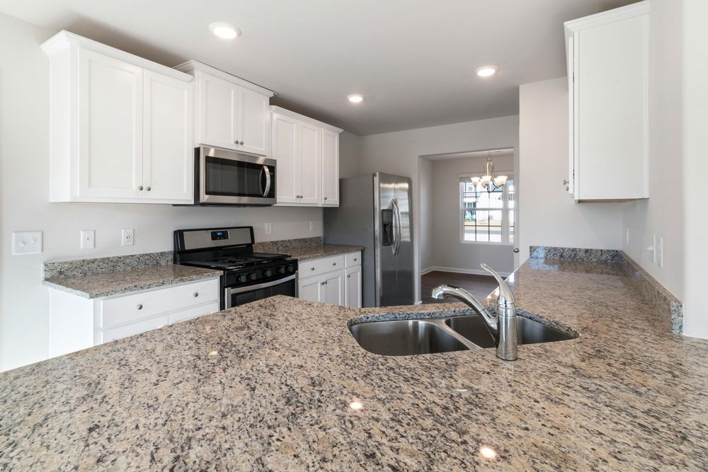 A kitchen with granite counter tops , stainless steel appliances , and white cabinets.