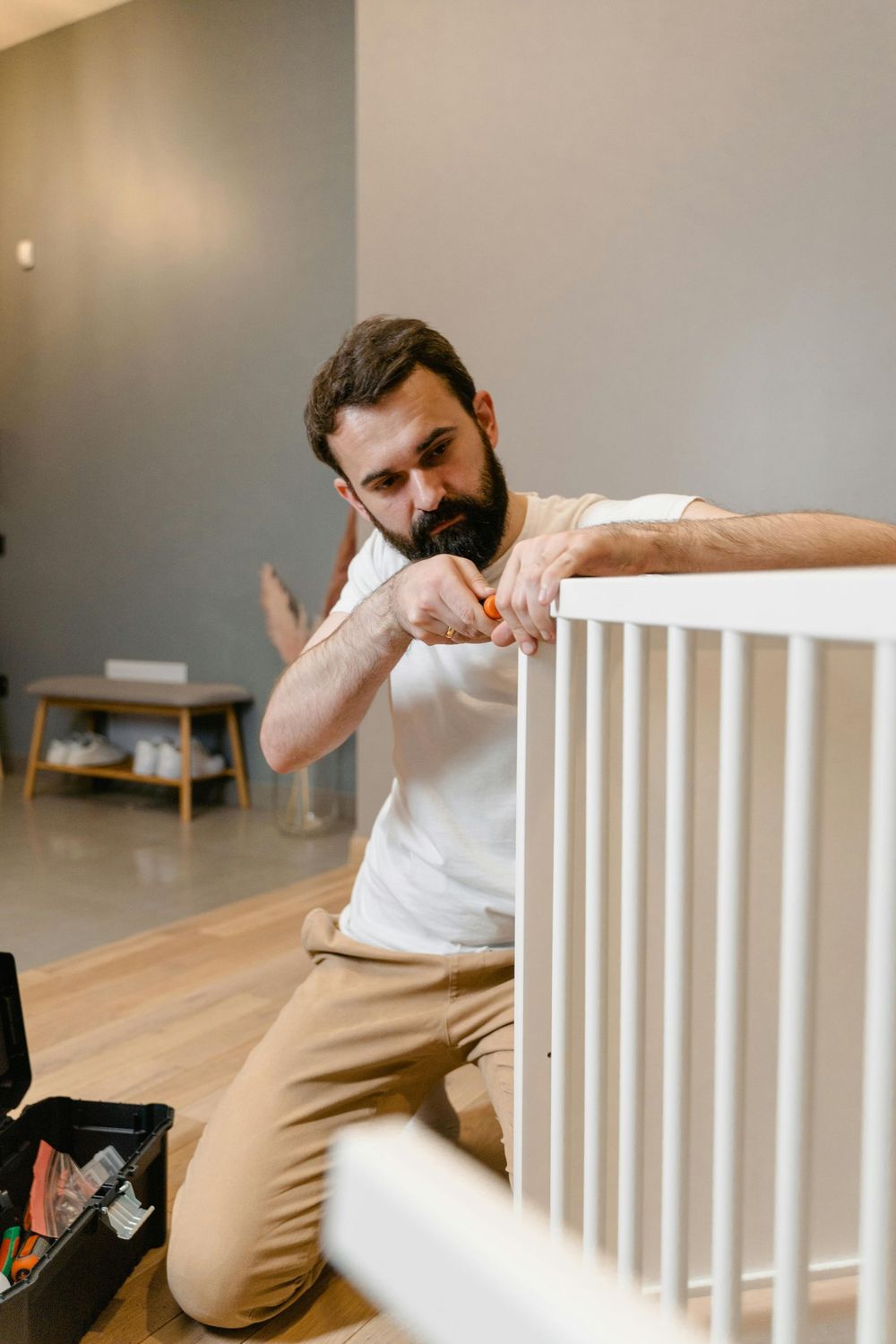 A man is kneeling on the floor fixing a baby crib.