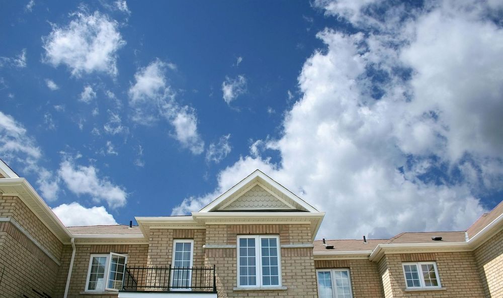 A brick house with a balcony against a blue sky with clouds