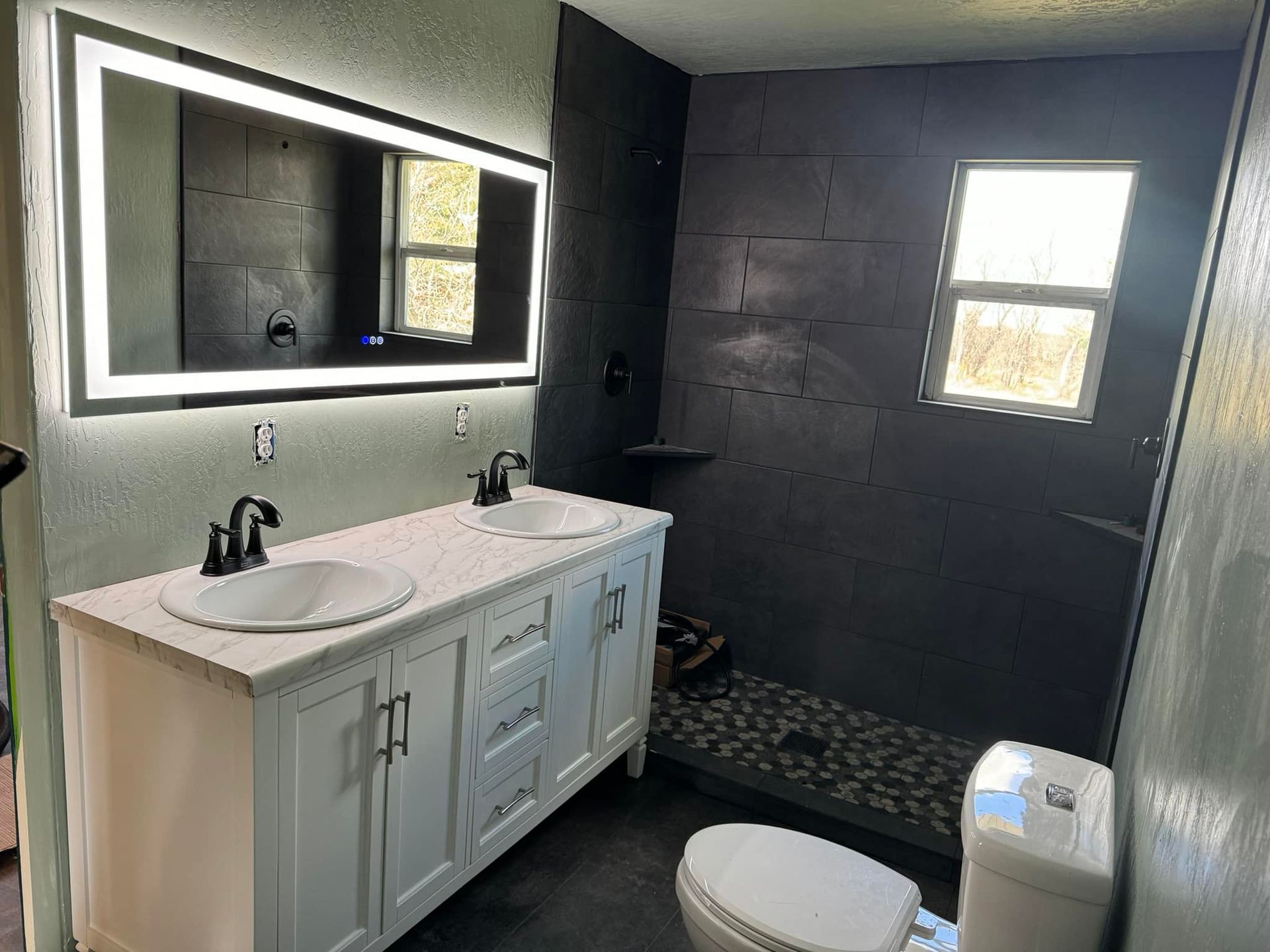 Modern bathroom with a white double vanity, large mirror, and dark gray tiled shower.