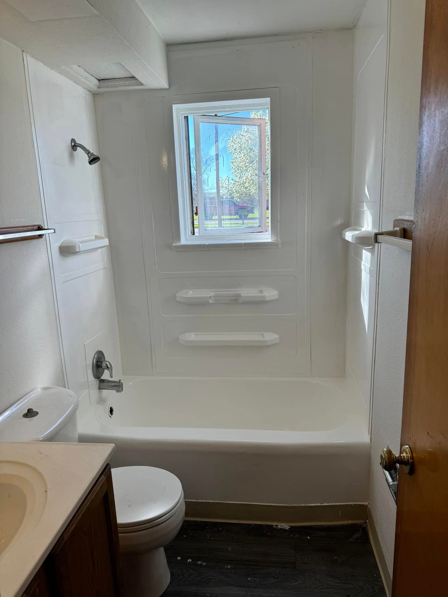 Bathroom with a white bathtub, toilet, and sink. A window provides natural light.