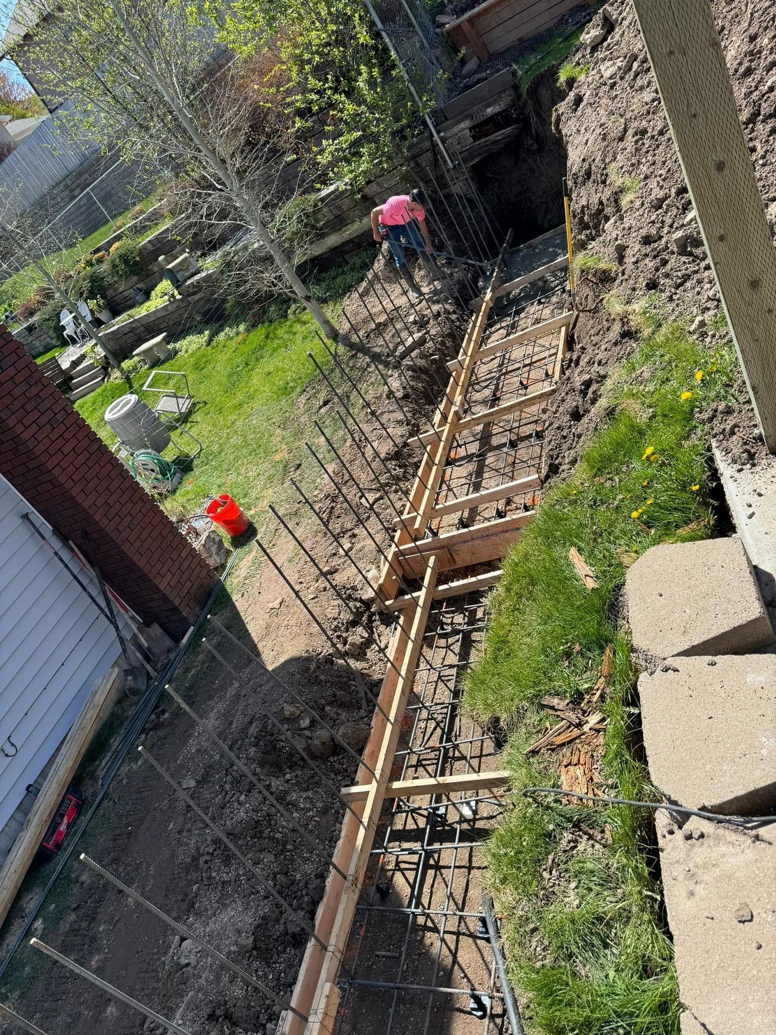 Construction of a concrete staircase in a yard; worker in pink shirt.